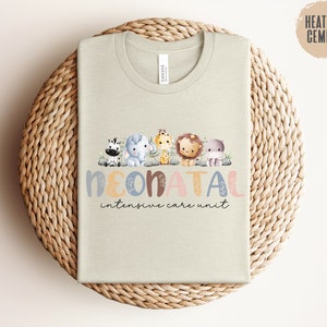 May include: A light beige t-shirt with a graphic of a line of cartoon animals and the text "NEONATAL intensive care unit".