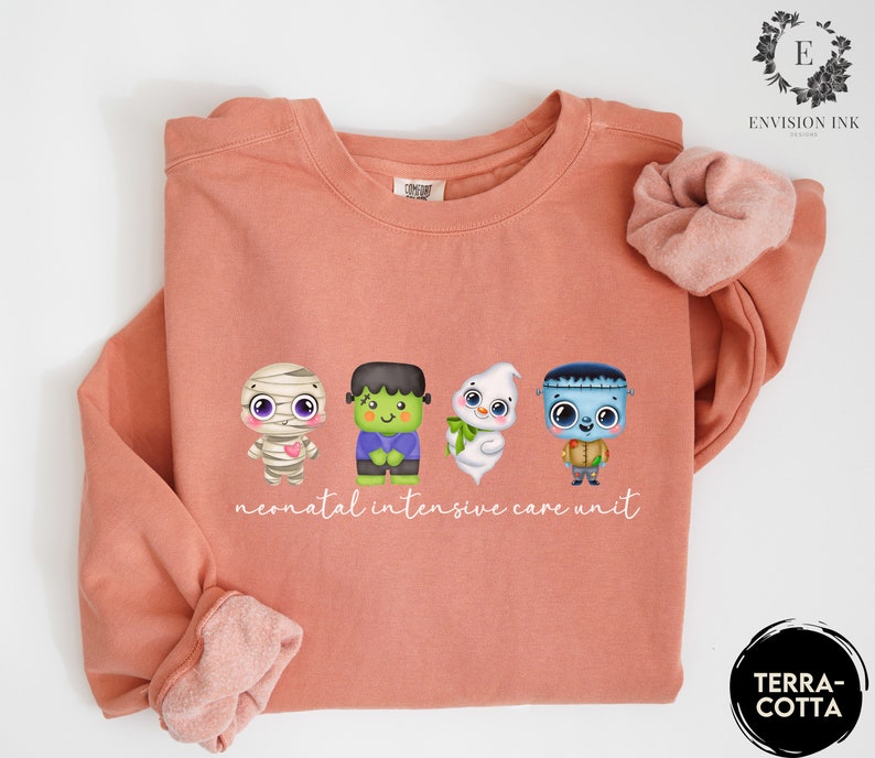 May include: A terracotta orange sweatshirt with a graphic of four cute cartoon monsters. The text "neonatal intensive care unit" is printed below the monsters.