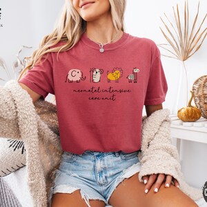 May include: A red t-shirt with a graphic of a series of animals, including an elephant, a bear, a lion, and a giraffe. The text "neonatal intensive care unit" is printed below the animals.