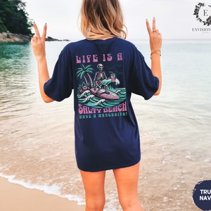 K&ouml;nnte beinhalten: Ein marineblaues T-Shirt mit einem Grafikdruck eines Skeletts auf einem Surfbrett mit dem Text "Life is a Salty Beach Have a Margarita!"