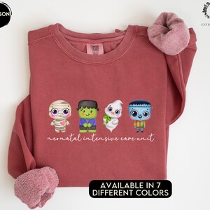 May include: A maroon sweatshirt featuring a graphic of four cartoon monsters and the text "neonatal intensive care unit". The sweatshirt is available in seven different colours.