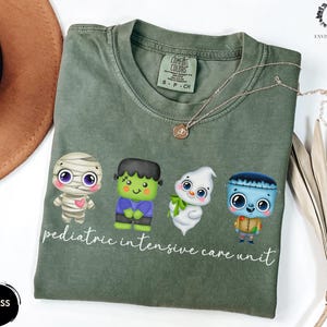 Pode incluir: Camiseta verde com um gr&aacute;fico de quatro monstros de desenho animado e o texto "pediatric intensive care unit".