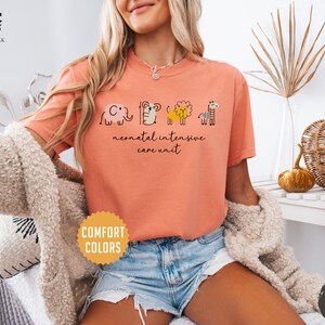 May include: A peach colored t-shirt with a graphic of a cartoon elephant, tiger, lion, and giraffe. The text "neonatal intensive care unit" is printed below the graphic.