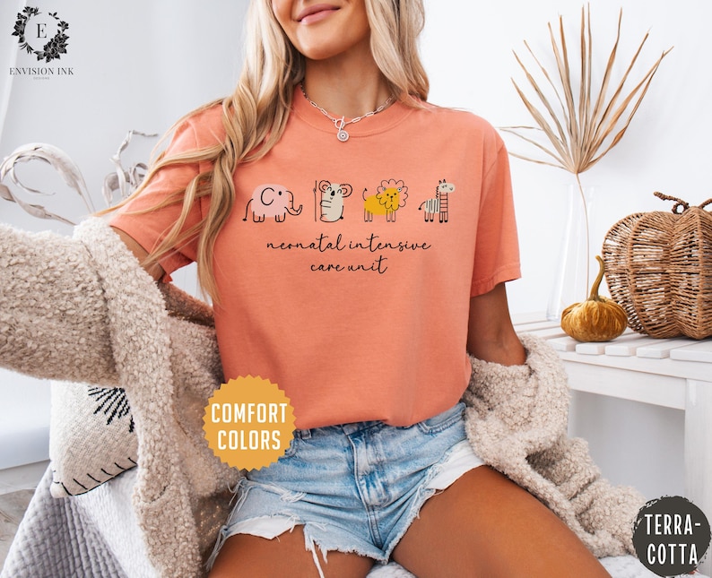 May include: A peach colored t-shirt with a graphic of a cartoon elephant, tiger, lion, and giraffe. The text "neonatal intensive care unit" is printed below the graphic.