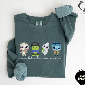 May include: A teal blue sweatshirt with a graphic of four Halloween-themed characters and the text "neonatal intensive care unit".