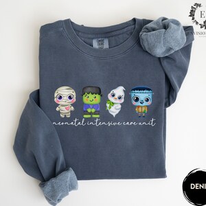 May include: A dark blue sweatshirt with a white graphic of four cartoon monsters and the text "neonatal intensive care unit".