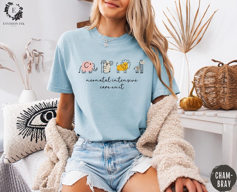 May include: A light blue t-shirt with a graphic of a line of animals, including an elephant, a giraffe, a lion, and a zebra. The text "neonatal intensive care unit" is printed below the animals.