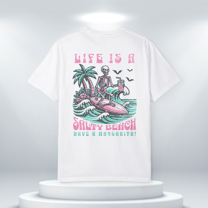 K&ouml;nnte beinhalten: Wei&szlig;es T-Shirt mit einem Grafikdruck eines Skeletts, das mit einer Margarita surft. Der Text "Life is a Salty Beach Have a Margarita!" ist auf dem T-Shirt aufgedruckt.