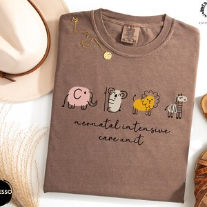 May include: A brown t-shirt with a graphic of a cartoon elephant, koala, lion, and zebra. The text "neonatal intensive care unit" is printed below the graphic.