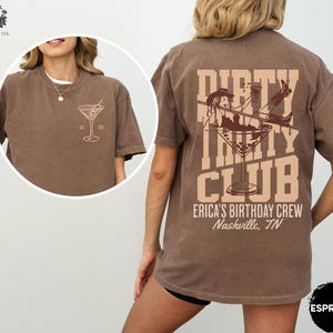 May include: Brown t-shirt with a graphic of a woman in a cowboy hat holding a martini glass with the text "Dirty Thirty Club" and "Erica's Birthday Crew Nashville, TN".