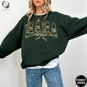 K&ouml;nnte beinhalten: Ein dunkelgr&uuml;ner Sweatshirt mit einem Tarnmuster-Druck "MAMA" und einer Schleife.