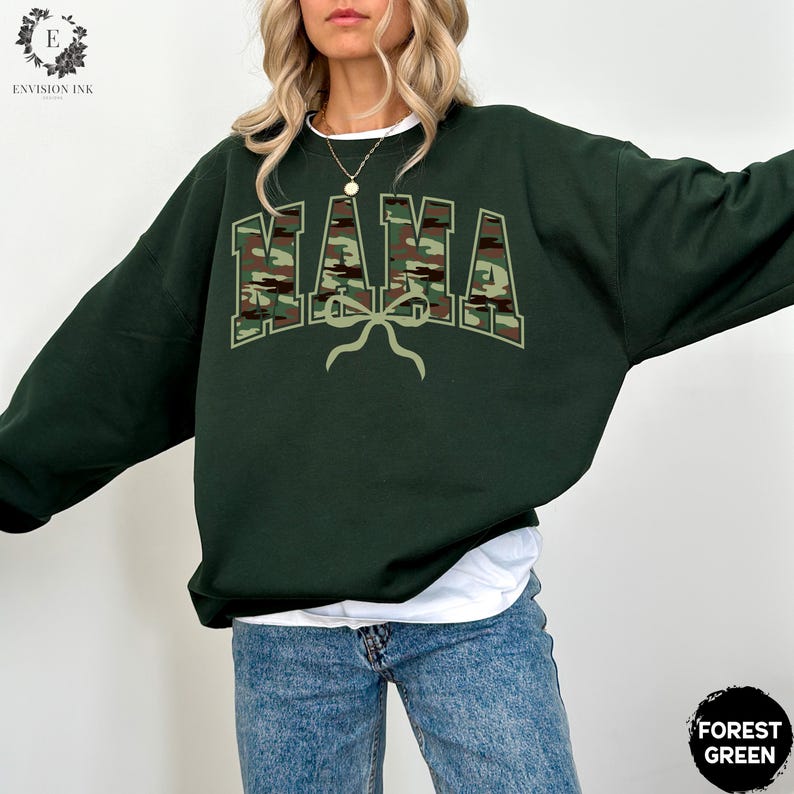 K&ouml;nnte beinhalten: Ein dunkelgr&uuml;ner Sweatshirt mit einem Tarnmuster-Druck "MAMA" und einer Schleife.