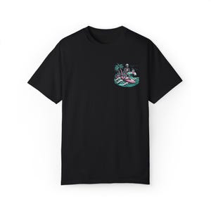 K&ouml;nnte beinhalten: Schwarzes T-Shirt mit einem Motiv eines Skeletts, das auf einem rosafarbenen Surfbrett mit einer Palme und einem Cocktail in der Hand surft.