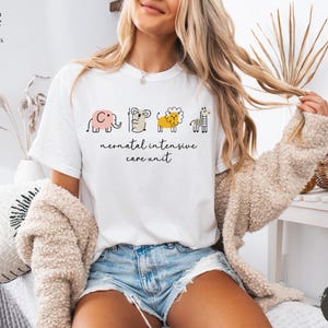 May include: White t-shirt with a graphic of a line of animals, including an elephant, a mouse, a lion, and a giraffe. The text "neonatal intensive care unit" is printed below the animals.