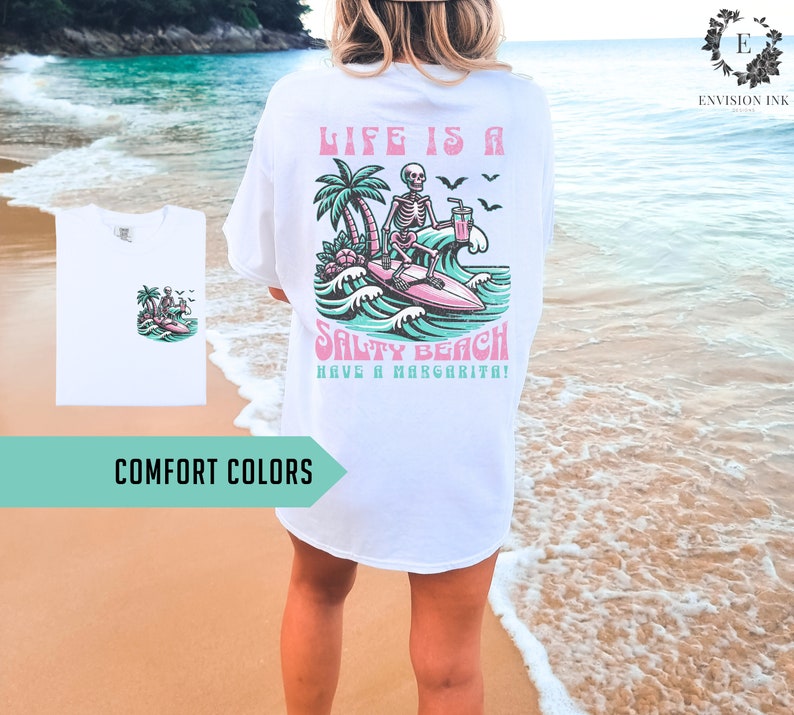 K&ouml;nnte beinhalten: Wei&szlig;es T-Shirt mit einem Grafikdruck eines Skeletts, das auf einer Welle surft, mit dem Text "Life is a Salty Beach Have a Margarita!"