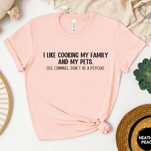 May include: A pink t-shirt with the text "I like cooking my family and my pets. Use commas. Don't be a psycho." printed in black.