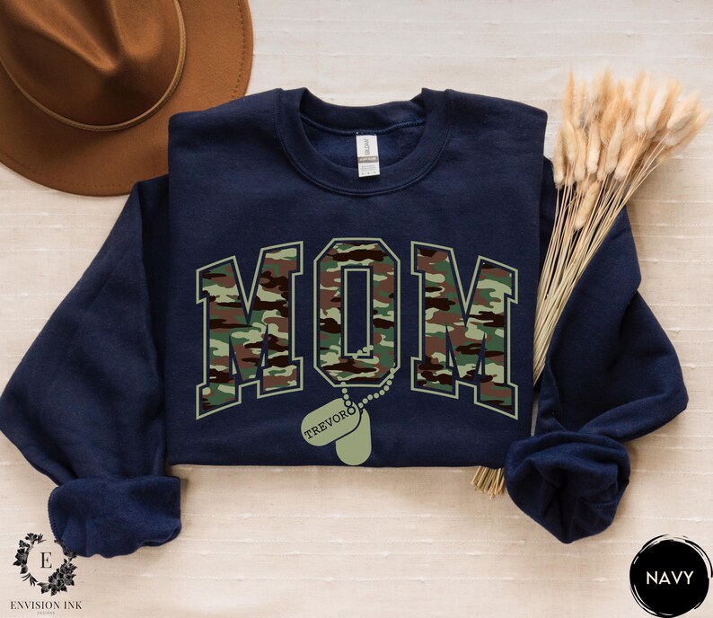 May include: Navy blue sweatshirt with a camouflage print of the word "MOM" and a dog tag with the name "TREVOR" printed on it.