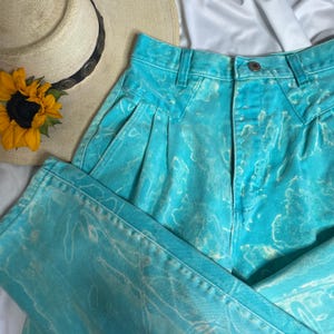 May include: High-waisted blue jeans with a tie-dye pattern in shades of turquoise and white.