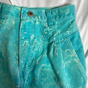 Op de afbeelding: Een lichtblauwe spijkerbroek met hoge taille en een wit tie-dye patroon. De broek heeft een knoopsluiting en riemlussen.