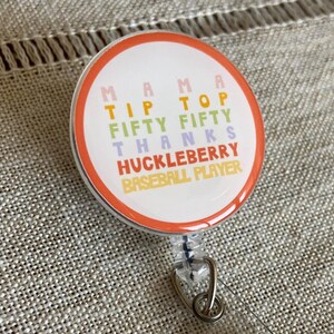 May include: A colorful badge holder with the text "Mama Tip Top Fifty Fifty Thanks Huckleberry Baseball Player".