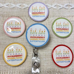 Può includere: Una collezione di porta badge rotondi e colorati. Ogni porta badge presenta il testo "MAMA TIP TOP FIFTY FIFTY THANKS HUCKLEBERRY BASEBALL PLAYER CATERPILLAR" con un bordo di colore diverso.