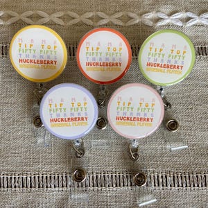 May include: Five colorful retractable badge holders with a white background and the text "Mama Tip Top Fifty Fifty Thanks Huckleberry Baseball Player".