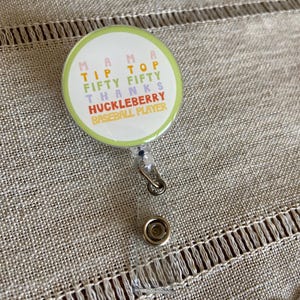 May include: A green, yellow, pink, and blue badge holder with the text "Mama Tip Top Fifty Fifty Thanks Huckleberry Baseball Player".