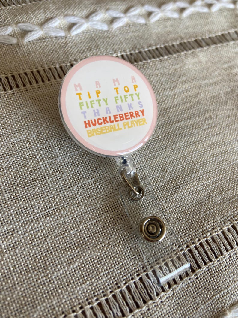 May include: A pink and white round badge with the text "Mama Tip Top Fifty Thanks Huckleberry Baseball Player" in rainbow colors.