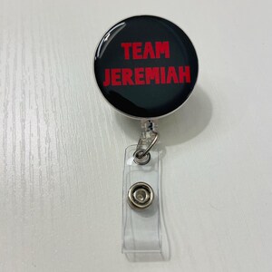 May include: A black retractable badge reel with the words "TEAM JEREMIAH" in red lettering. The reel has a clear plastic strap with a snap closure and a metal clip.