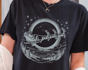 Könnte beinhalten: Ein schwarzes Kurzarm-T-Shirt mit einem hellgrauen Grafikdruck, der den Weihnachtsmann in einem von Rentieren gezogenen Schlitten vor einem großen Mond zeigt. Das Design umfasst eine verschneite Waldlandschaft und Schneeflocken.