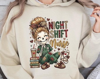 Könnte beinhalten: Ein beigefarbener Kapuzenpullover mit einer Grafik eines Skelett-Krankenpflegers mit Dutt, der grüne Arbeitskleidung und Leopardenmuster-Accessoires trägt. Der Text lautet NIGHT SHIFT Nurse, ergänzt durch einen Kaffeebecher, Bücher und ein Stethoskop.