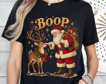 Könnte beinhalten: Ein schwarzes Kurzarm-T-Shirt mit einem Grafikdruck, der den Weihnachtsmann zeigt, wie er die rote Nase eines Rentiers berührt. Über den Figuren steht das Wort BOOP in einer goldenen, stilisierten Schrift. Das Design enthält Sterne und einen Kranz.