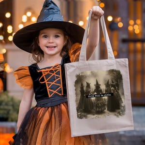 May include: A young girl in a black witch costume and hat holds a beige tote bag. The bag features a sepia-toned image of witches with the text "Girls will be girls."