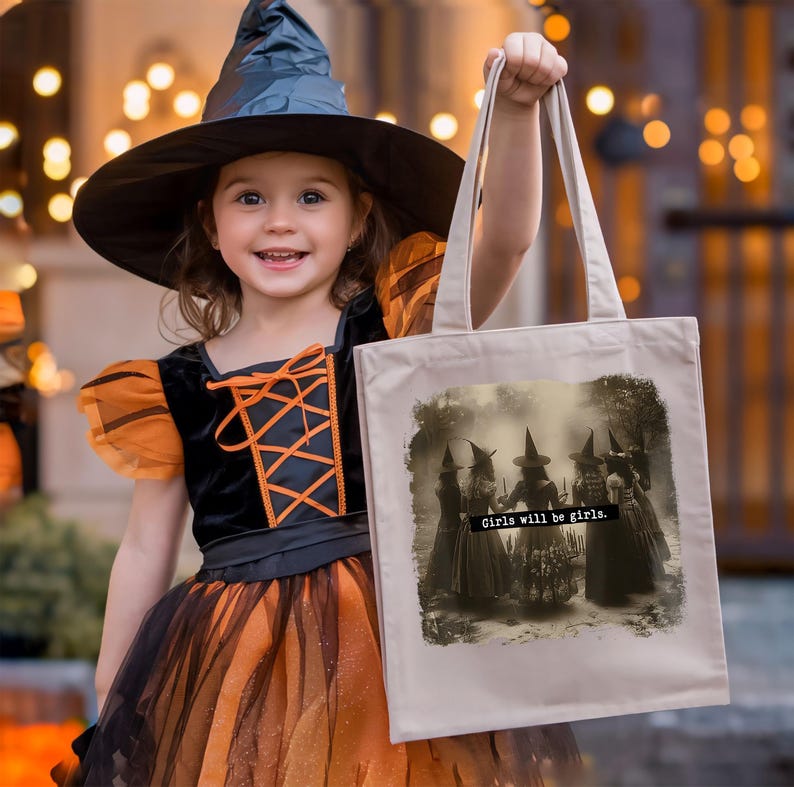 May include: A young girl in a black witch costume and hat holds a beige tote bag. The bag features a sepia-toned image of witches with the text "Girls will be girls."
