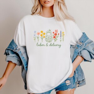 May include: White t-shirt with a green floral design and the text "labor & delivery".