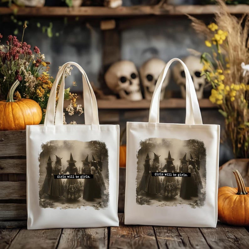 May include: Two off-white tote bags with cream-colored handles. Each bag features a sepia-toned image of witches and the text "Girls will be girls." Pumpkins and fall foliage are in the background.