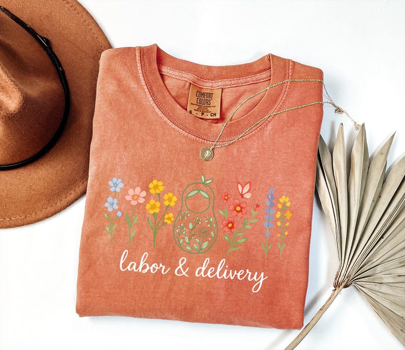 May include: A peach-colored t-shirt with a floral design and the text "labor & delivery".