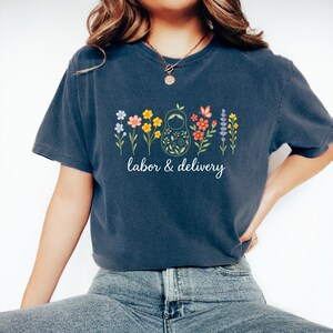 May include: A navy blue t-shirt with a graphic of a nesting doll surrounded by colorful flowers and the text "labor & delivery".