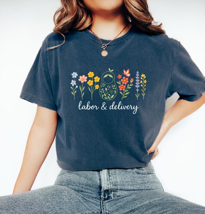 May include: A navy blue t-shirt with a graphic of a nesting doll surrounded by colorful flowers and the text "labor & delivery".