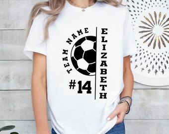 May include: White t-shirt with a soccer ball graphic, the text "TEAM NAME" and the name "ELIZABETH" in black. The number "14" is below the soccer ball. The shirt is worn by a person.