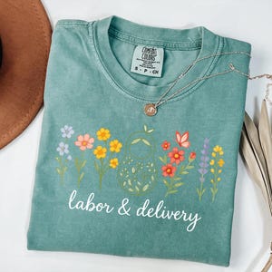 May include: A teal blue t-shirt with a floral design and the text "labor & delivery" in white.