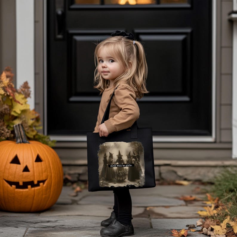May include: A black tote bag with the text "Girls will be Girls" and a sepia-toned image of witches. A carved pumpkin and a young child are in the image, suggesting a Halloween theme.