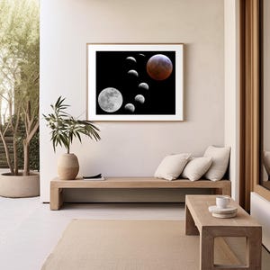 May include: A framed print of a black and white photograph of a lunar eclipse. The image shows the moon in various phases, including a full red moon. The print is hanging on a white wall in a modern living room setting.