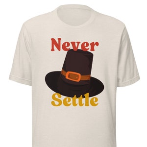 May include: A white t-shirt with the text "Never Settle" in red and orange letters. A black pilgrim hat with an orange buckle is centered above the text.