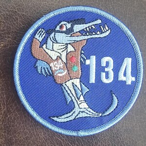 May include: Blue embroidered patch with a cartoon alligator wearing a brown vest and a green tie. The alligator is holding a sign that says "134".