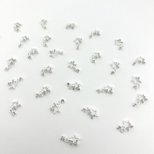 May include: A scattering of silver-toned metal charms shaped like stars with rhinestones. Each charm has a chain of three stars.