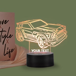 Könnte beinhalten: Eine weiße Umrandung eines Autos mit schwarzem Sockel, das Auto wird von innen mit orangefarbenem Licht beleuchtet. Der Sockel hat einen Schalter an der Seite und die Worte "YOUR TEXT" sind auf der Vorderseite aufgedruckt.