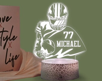 Pode incluir: Silhueta branca de um jogador de futebol americano segurando uma bola de futebol com o número 77 e o nome Michael na camisa. A silhueta está em uma base branca com uma superfície texturizada.