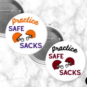 May include: White button pins with the text "practice SAFE SACKS" and football helmet graphics in orange and maroon. The pins have a silver metal backing and are displayed on a marble background.