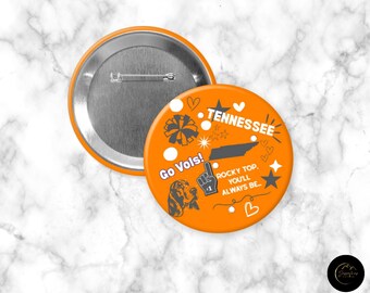 Könnte beinhalten: Oranger Button mit dem Wort "Tennessee" und einer Kartenumriss, sowie dem Text "Go Vols!" und "Rocky Top, You'll Always Be." Enthält eine Illustration eines Bloodhound und andere Grafiken. Der Knopf hat einen Durchmesser von etwa 7,6 cm.